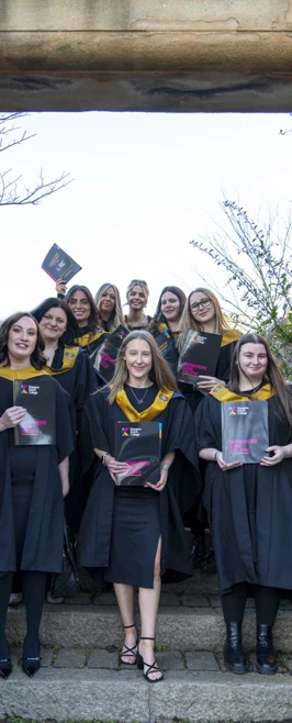 Group of smiling graduates posing with certificates outside under a stone archway. Group of smiling graduates posing with certificates outside under a stone archway.
